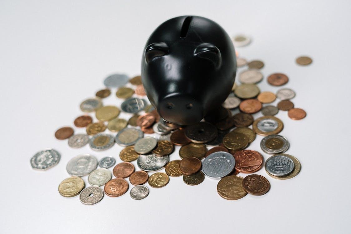 Free Black piggy bank surrounded by a variety of coins on a white surface, symbolizing savings and finance. Stock Photo