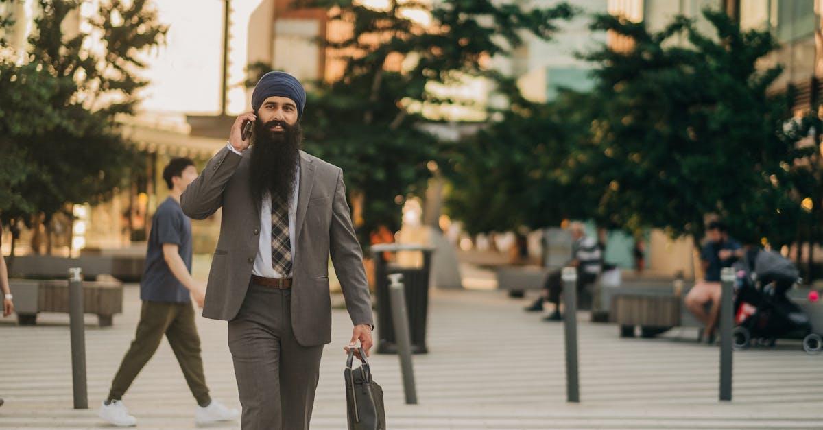 A businessman in a suit and turban walking confidently outdoors while talking on the phone.