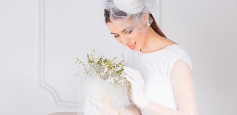 A person wearing a white dress and gloves holding a bouquet of flowers Description automatically generated