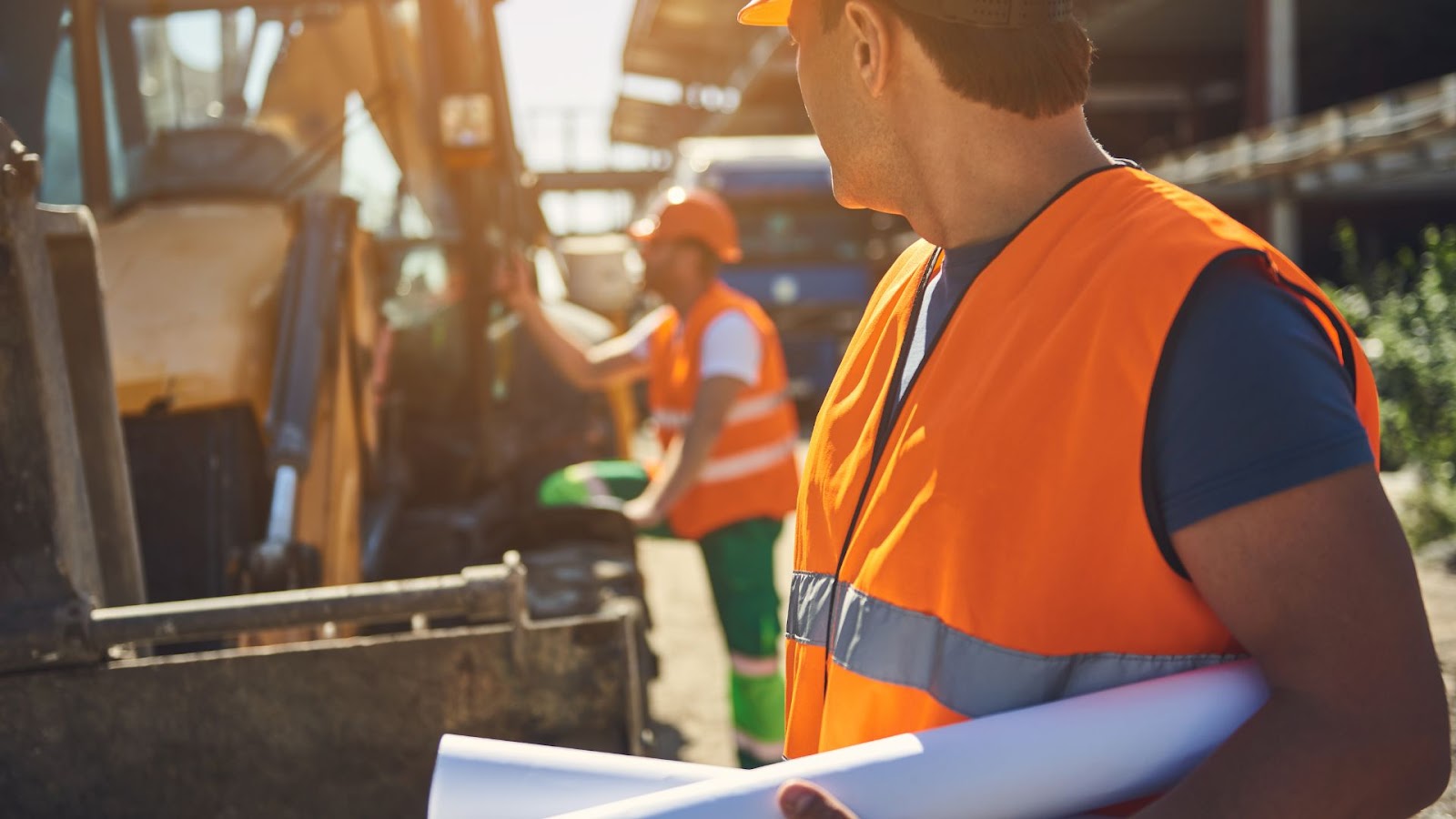 Construction workers holding blueprints in front of a bulldozer.