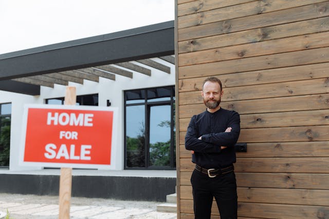 Person standing outside fo house with for sale sign