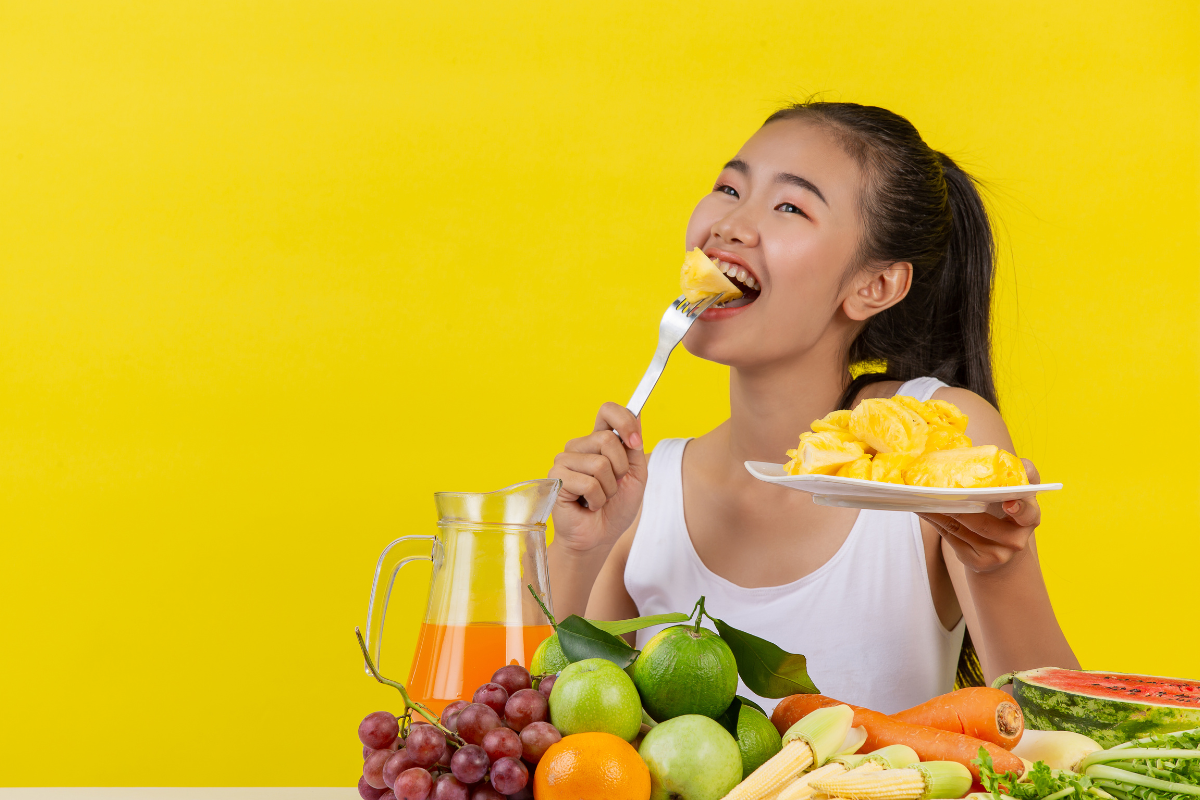 orang yang memakan buah di depan meja yang penuh dengan sayur dan buah