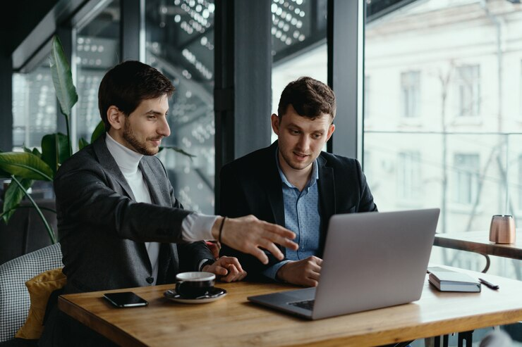 Two businessmen pointing at a laptop screen while discussing something