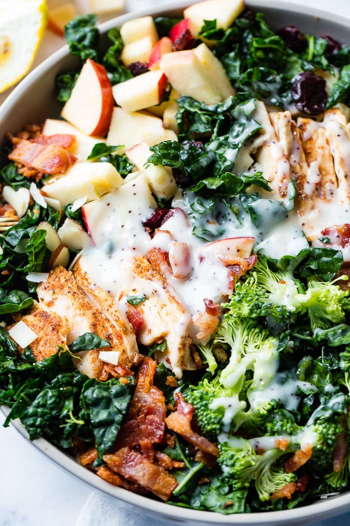 A photo of a kale salad loaded with apples, bacon, cranberries and smoked chicken topped with a poppy seed dressing.