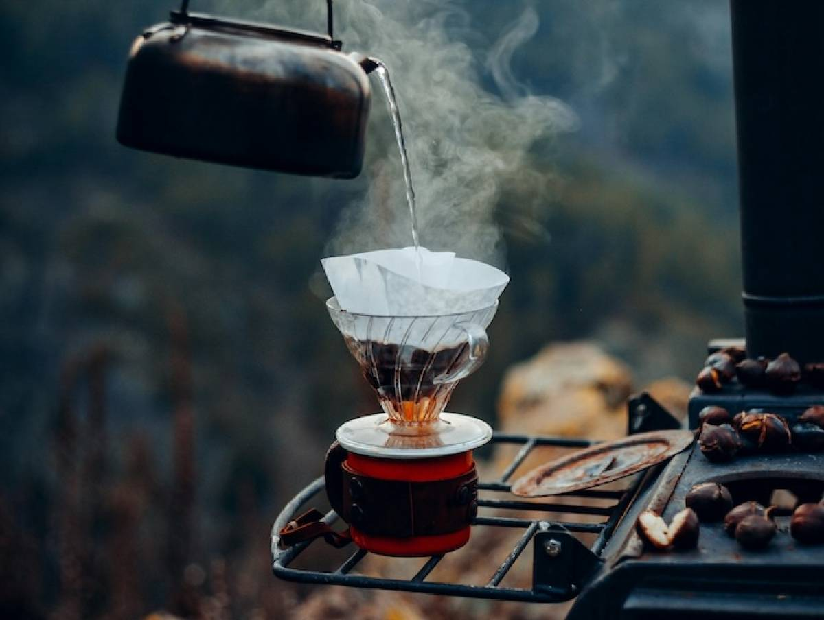 A black kettle pours water into a glass cup outdoors