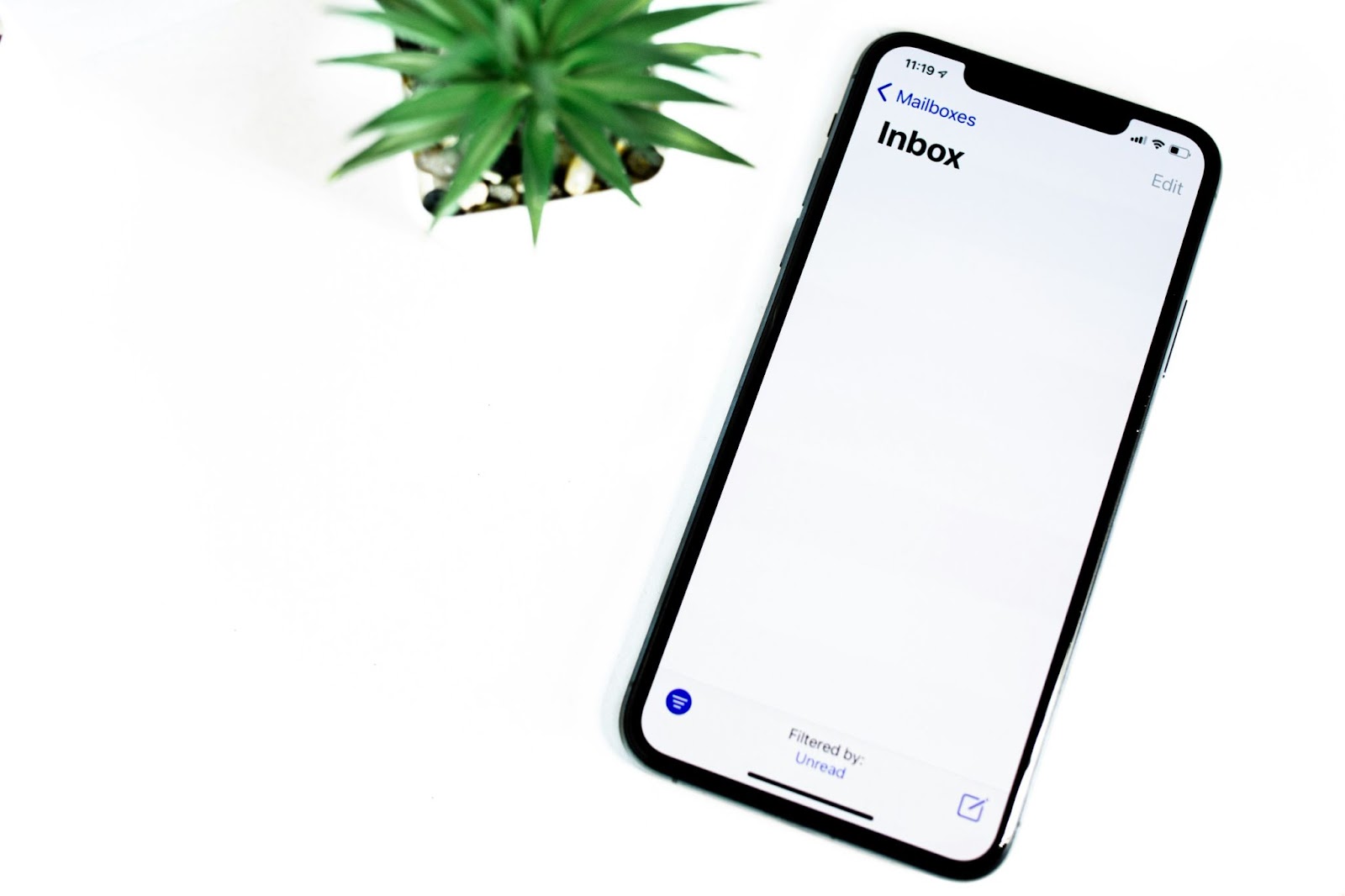 Smartphone displaying an empty email inbox screen, placed on a white surface next to a small green plant