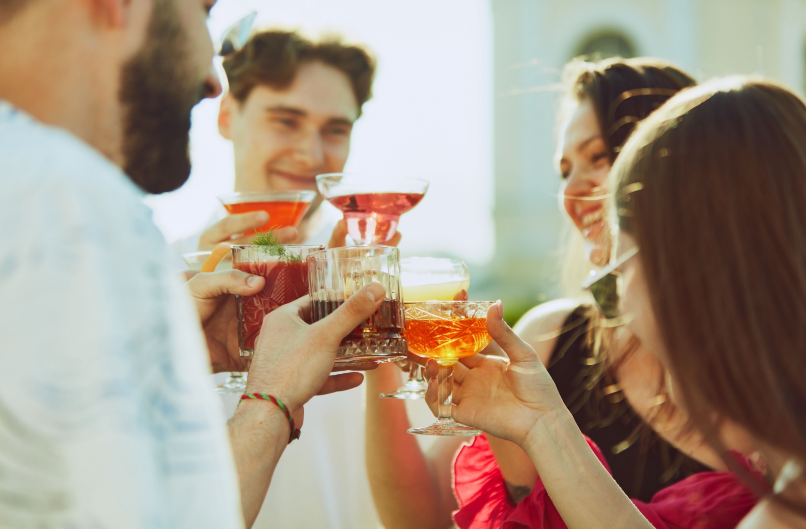 A friend group socializing and cheersing their beverages while maintaining physical distance from their faces.