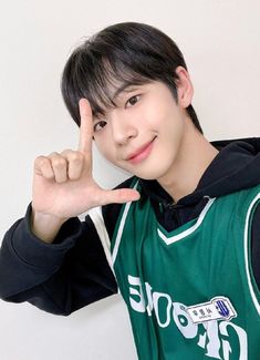 This contain Seo Jeongwoo  in a green and black hoodie making the peace sign with his hand