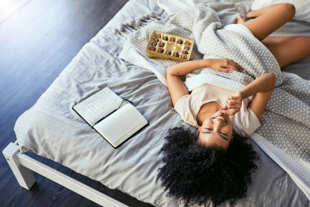 A woman smiling peacefully while lying in bed, looking relaxed and relieved after finding PMS symptom relief.
