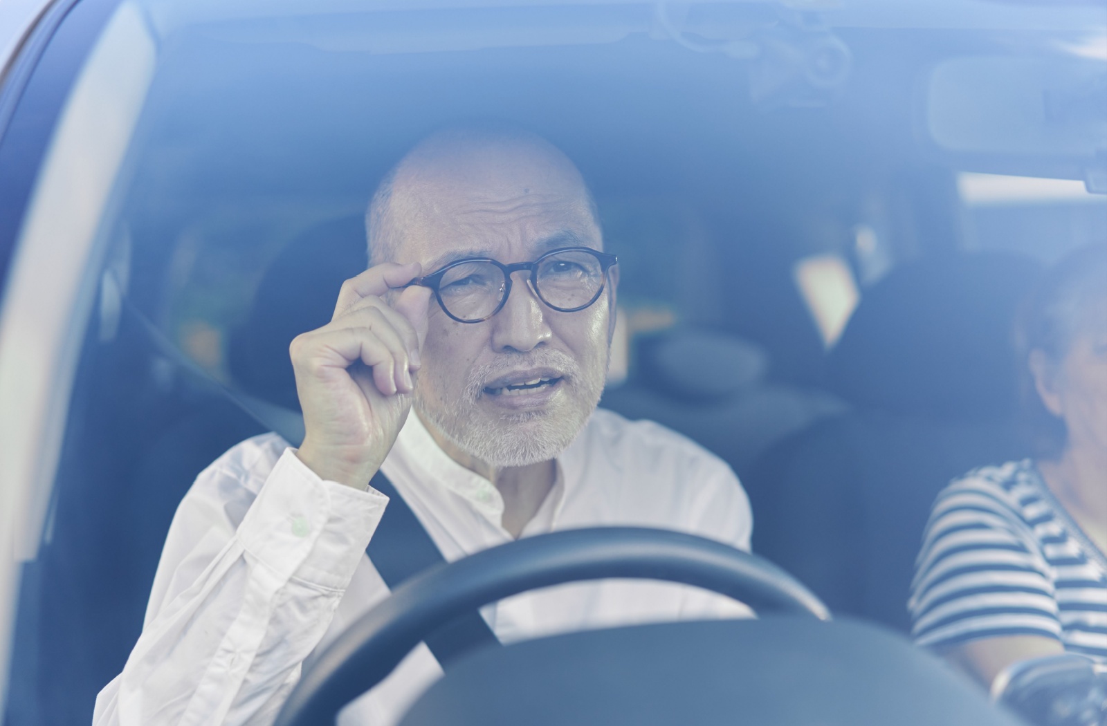 Elderly man adjusting his glasses while driving.