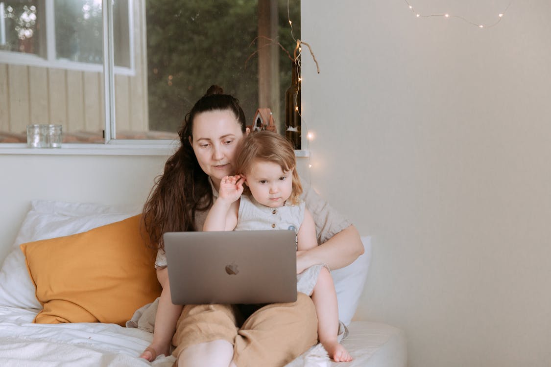 Free Adult woman with preschool girl in dress spending time together on bed using laptop Stock Photo