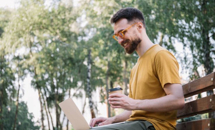 When to wear blue light glasses: A man sitting on a park bench with his laptop wearing orange-colored glasses