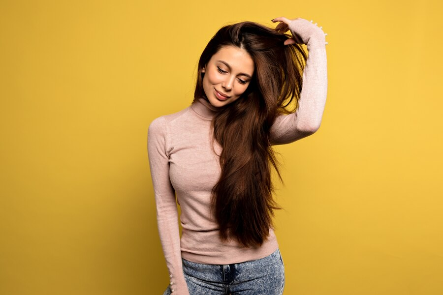 Pretty girl in pink pullover straightens her shiny hair