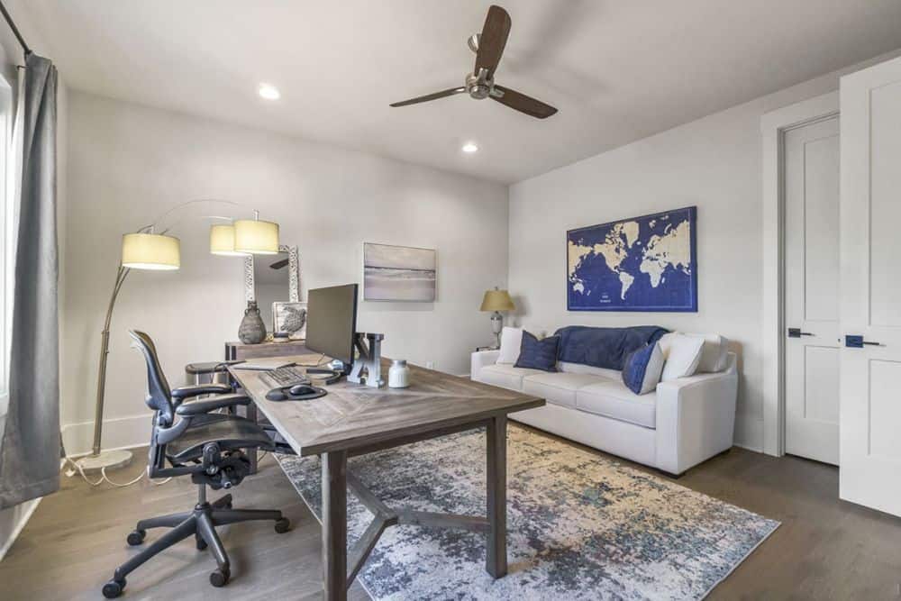The home office is furnished with a white sectional and a wooden desk paired with a black swivel chair.