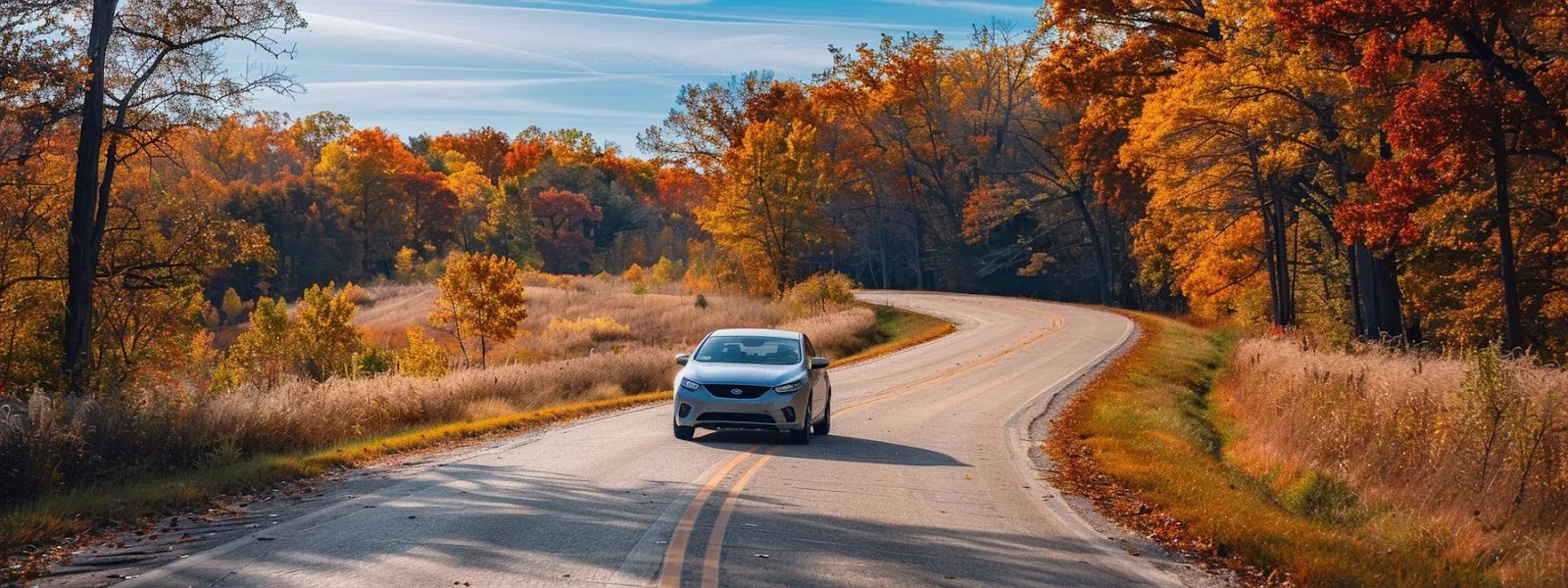 a sleek silver car driving confidently down a winding oklahoma road, surrounded by colorful foliage and under a clear blue sky, embodying the importance of comprehensive car insurance coverage in the state.