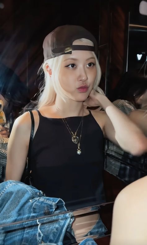 This contain an image of Rosé with white hair wearing a black top and jeans sitting in front of a mirror