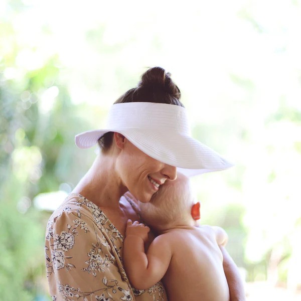 Woman with white wide brim sun visor by SwimZip holds her baby—Best hats for sun protection (a guide)