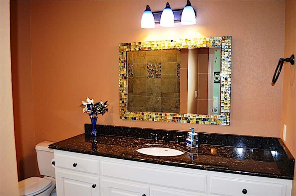 This bathroom offers a toilet and a large sink vanity paired with a colorful mirror and glass sconces.