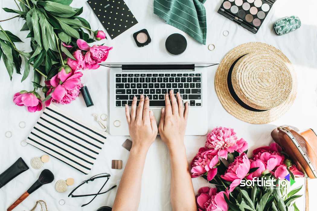 Hands typing on a laptop surrounded by flowers and accessories