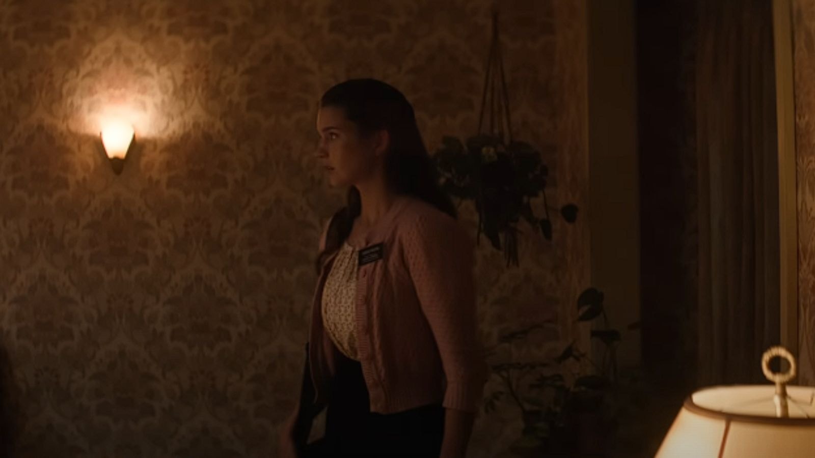 Chloe East cautiously walking through a dimly lit room.