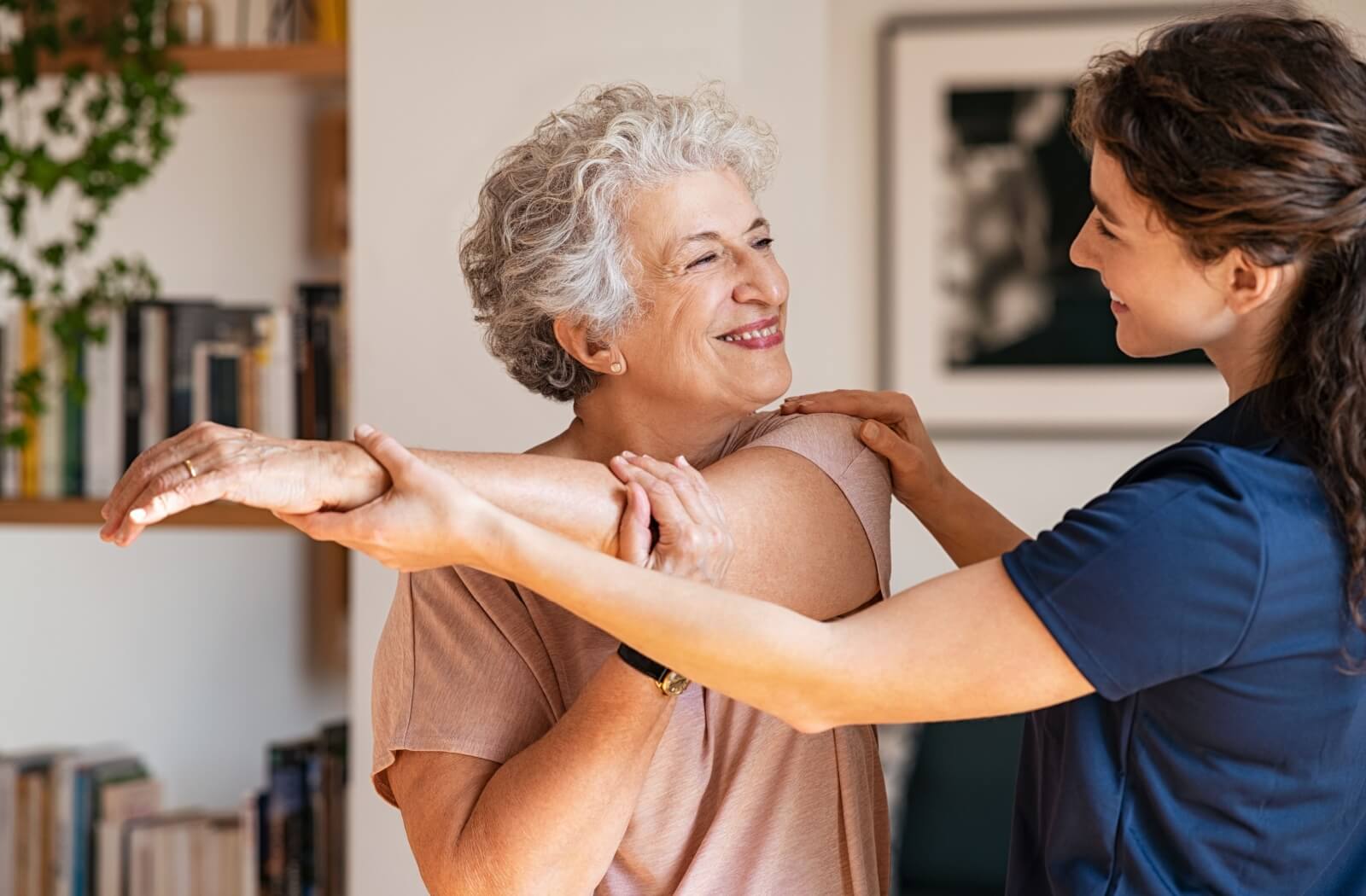 A compassionate caregiver in a personal care community assists a senior with gentle stretching.