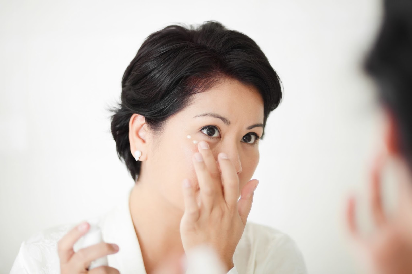 A woman uses a mirror to apply cream around her eyes to treat dryness