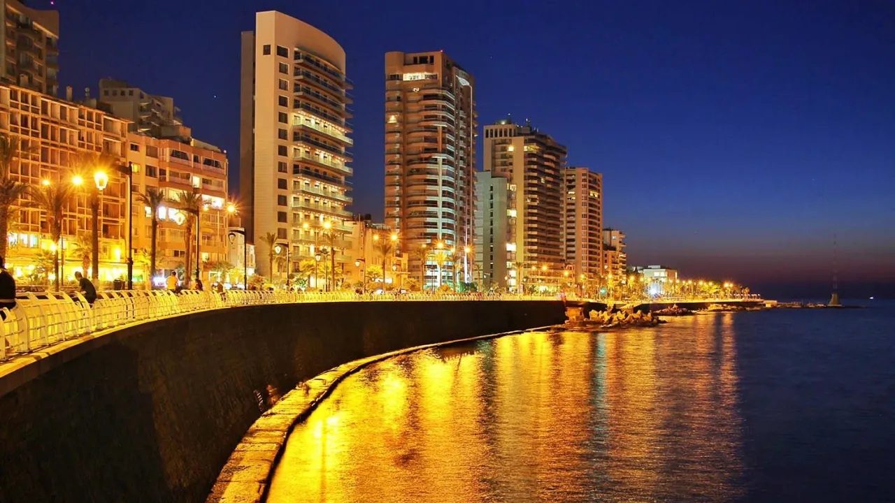 Beirut waterfront at night with modern high-rise buildings lit up along the Mediterranean Sea under a deep blue sky.