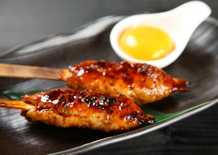 Two tsukune yakitori sticks with raw egg yolk on the side