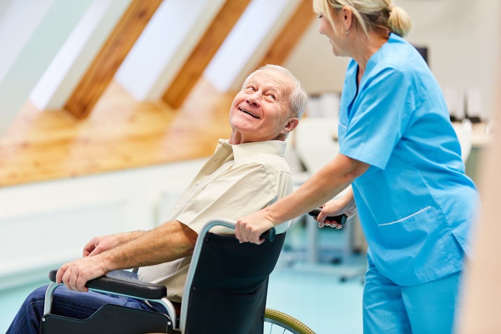 an assisted living staff member pushes a man in a wheelchair who looks back and smiles at her.