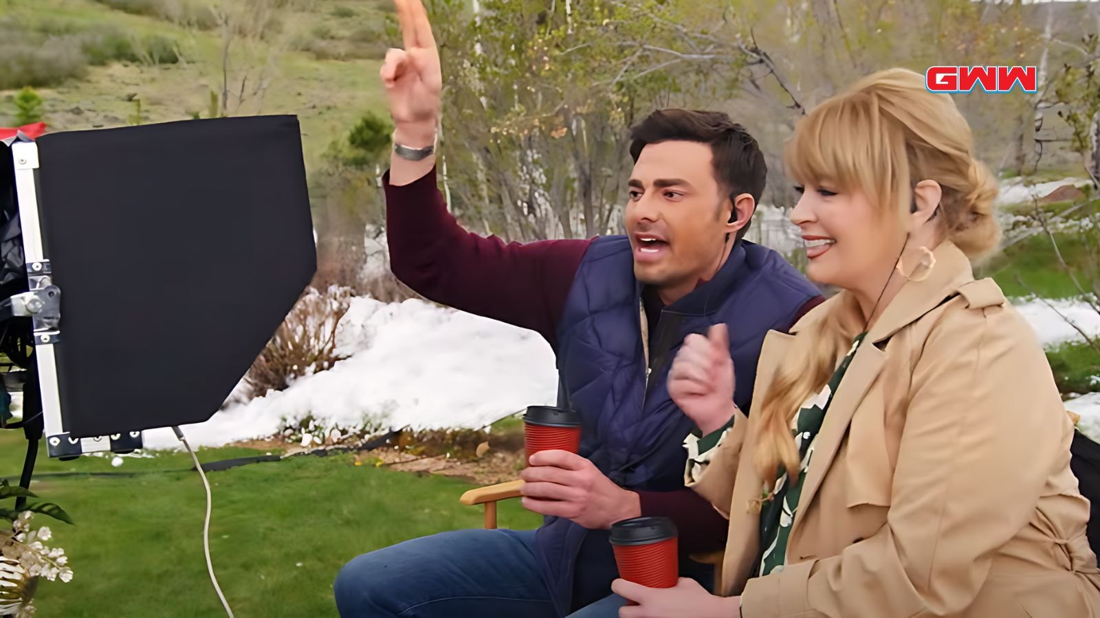 Jonathan Bennett and Melissa Peterman in coats direct a scene outside with headsets and coffee.