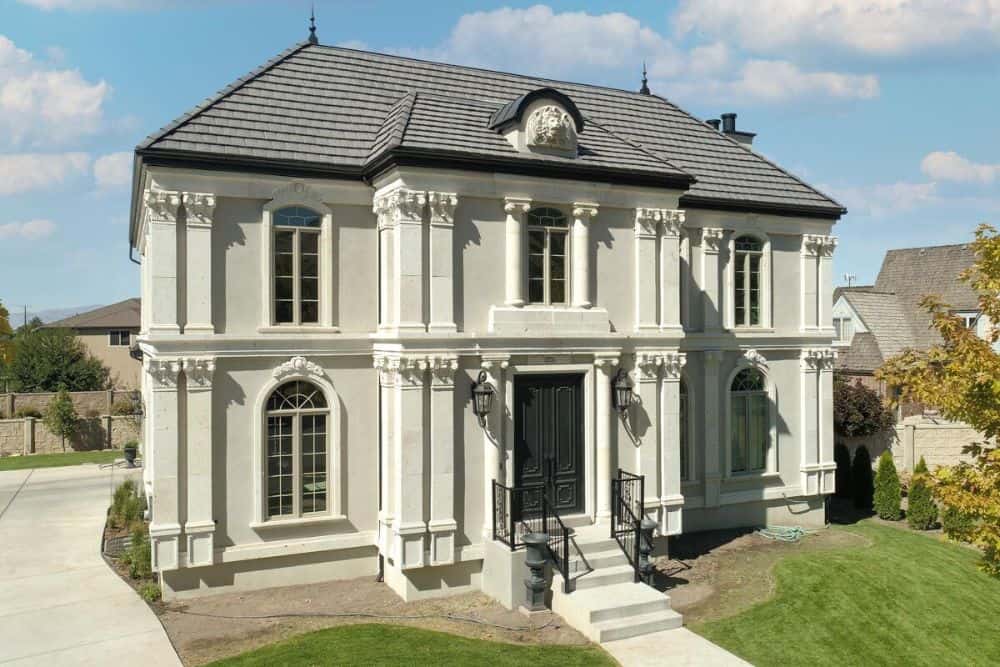 Front exterior view showing the hipped rooflines, intricate columns, and home entry bordered by wrought iron railings.
