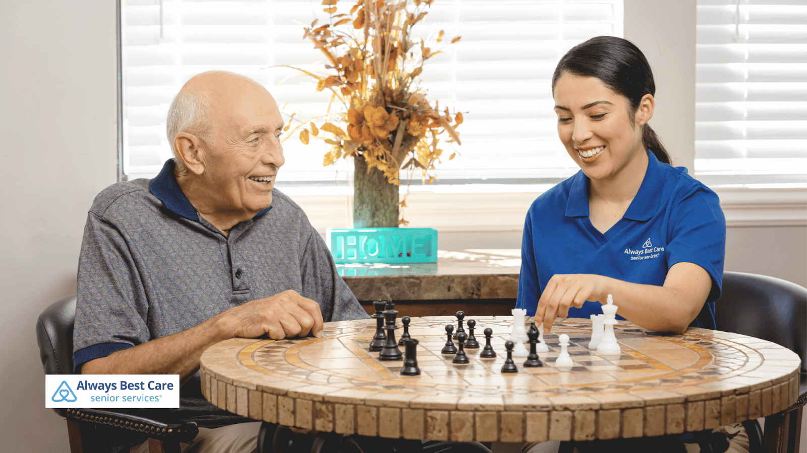 This image depicts a senior man playing chess with his caregiver