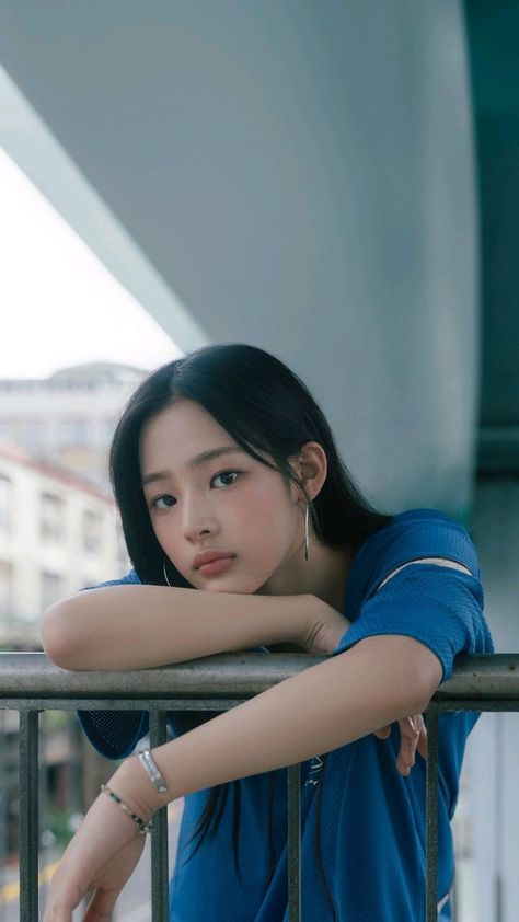 This contains an image of Minji wearing a blue polo and resting her face in a stair