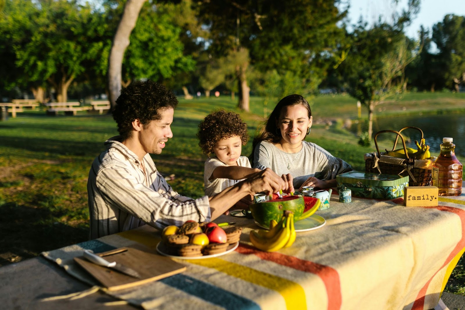 A family enjoying a picnic at a park, sharing fresh fruit and snacks at a table covered with a colorful blanket.