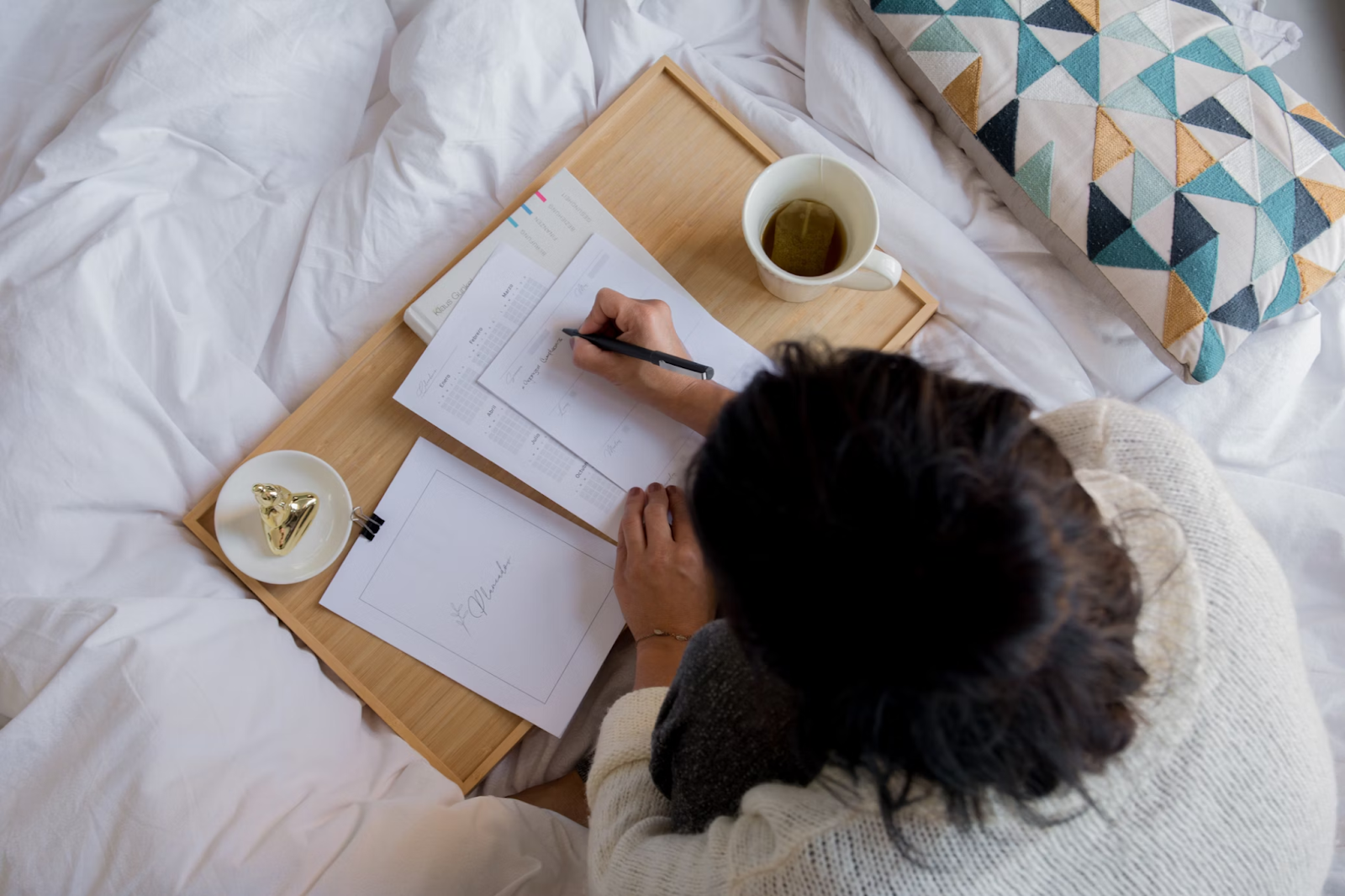 personne écrivant sur papier blanc à côté tasse en céramique blanche sur textile blanc