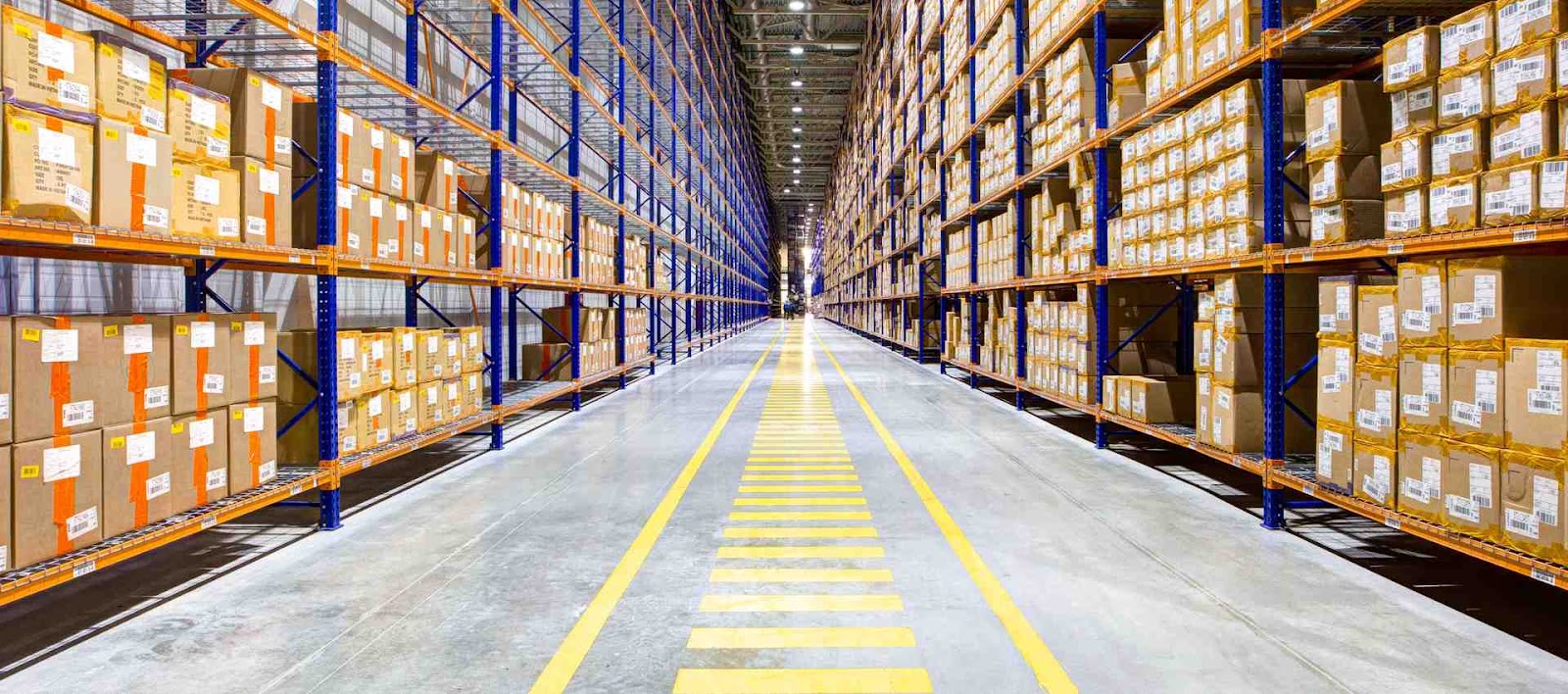 A clean warehouse aisle lined with tall shelves stocked with boxes and marked by yellow floor stripes.