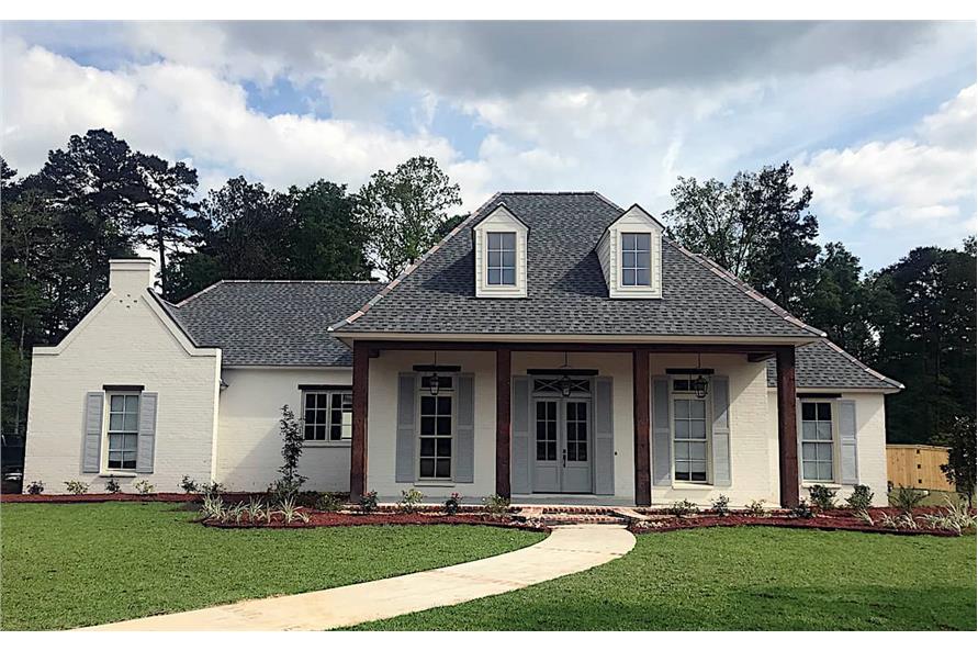 Front exterior view with hipped rooflines, shuttered windows, and a covered porch complemented with a brick stoop and curved paving.