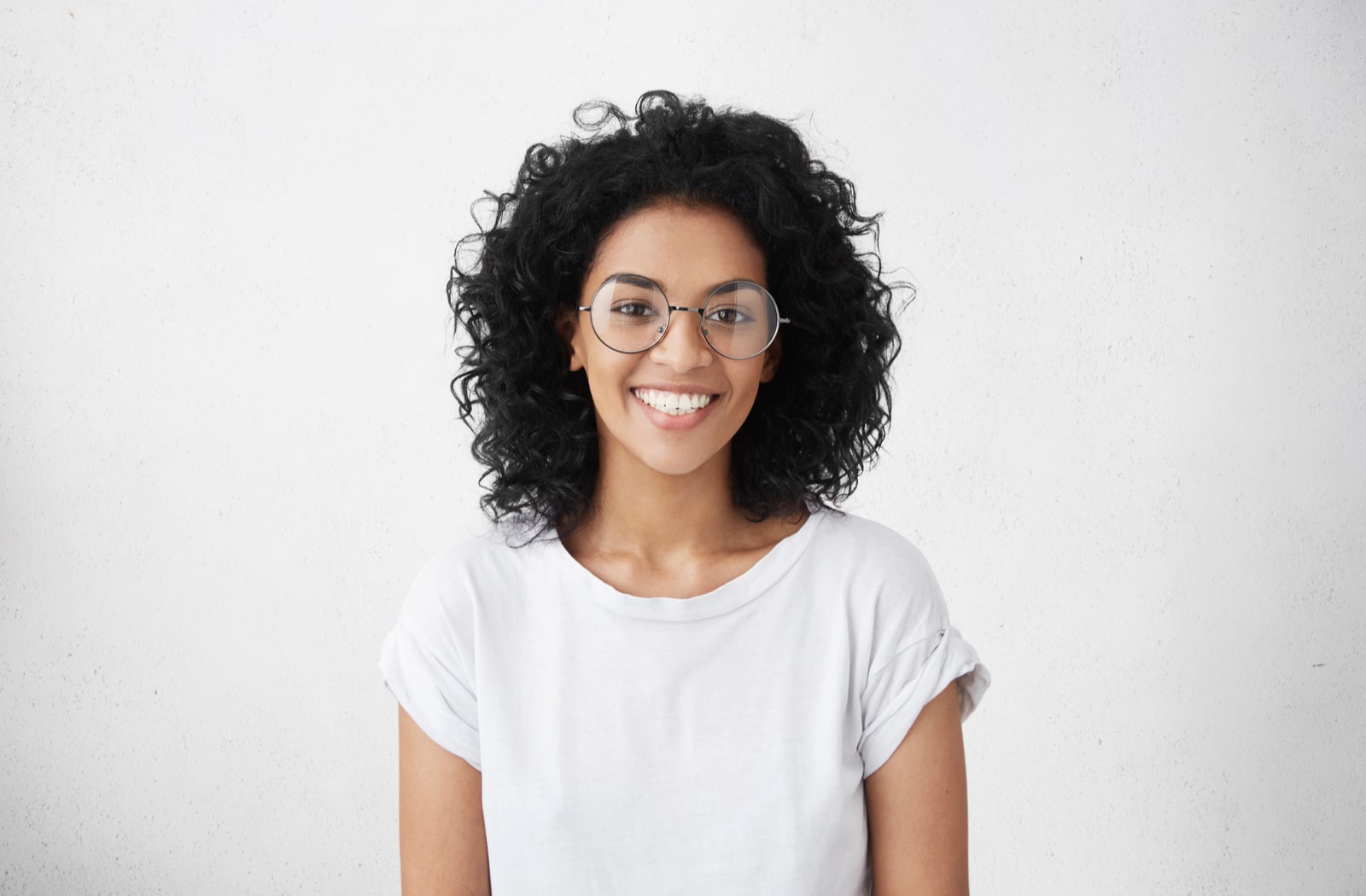 smiling young woman with voluminous black hair wearing large round glasses.