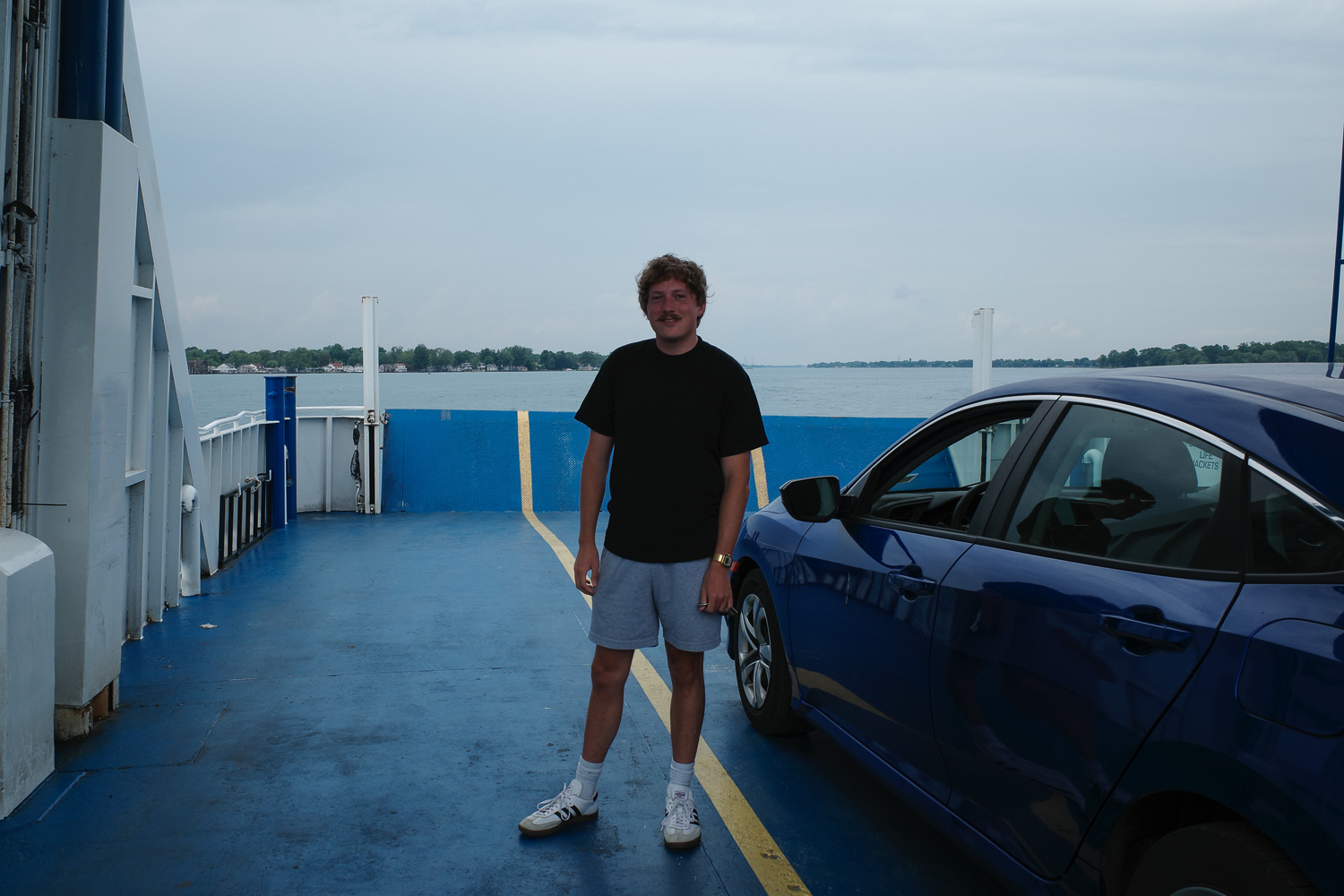 Bobby Mars smiling next to blue car on ferry mid-transit.