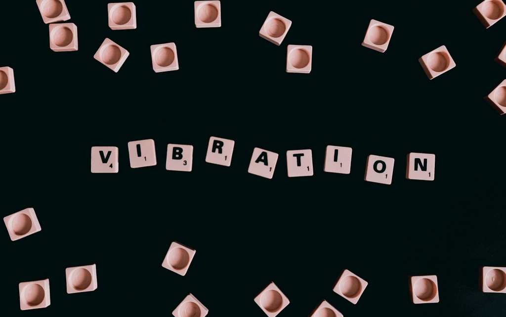 Scrabble tiles arranged to spell the word "VIBRATION" on a black background