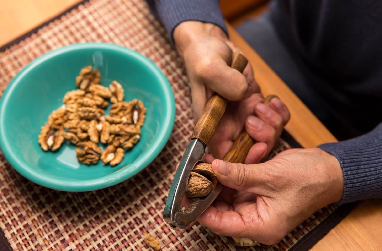 A close-up image of a senior preparing a heart-healthy snack by cracking walnuts.