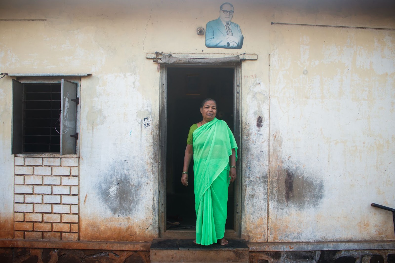 Photo of a woman in a green sari standing in the doorway of a home