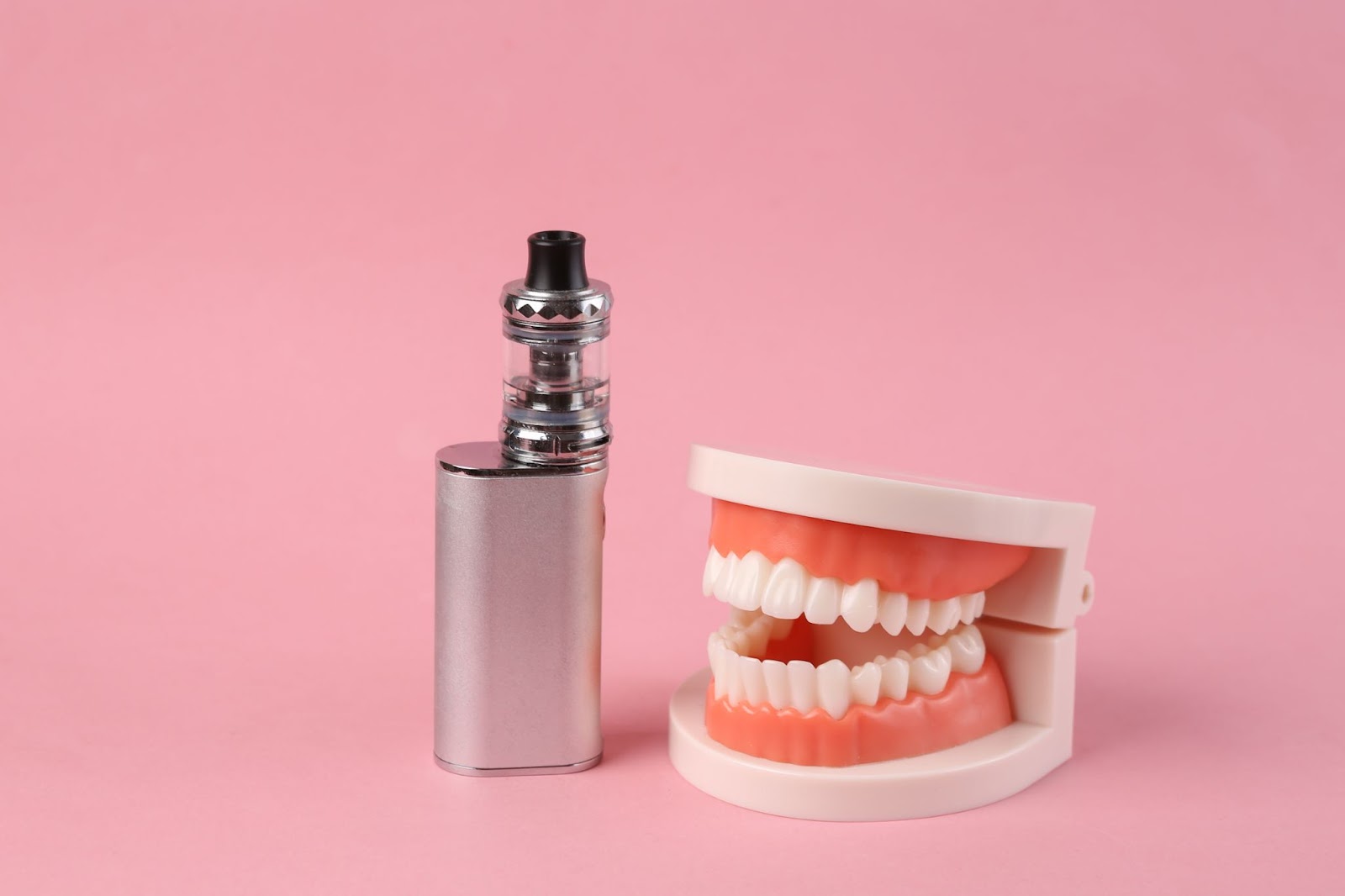  A dental jaw model next to a vape device on a pink background.