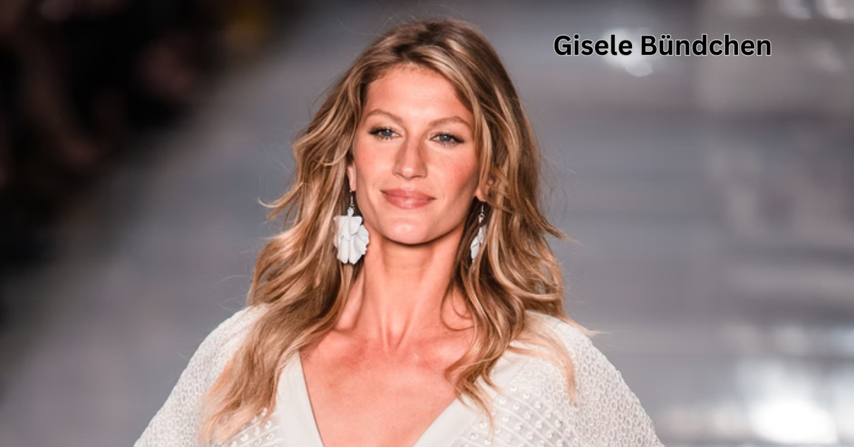 Gisele Bündchen walking on a runway, dressed in a light, textured outfit. She has long, wavy blonde hair and wears large floral earrings. Her expression is serene, and the background is blurred with a soft focus, emphasizing her as the central figure.