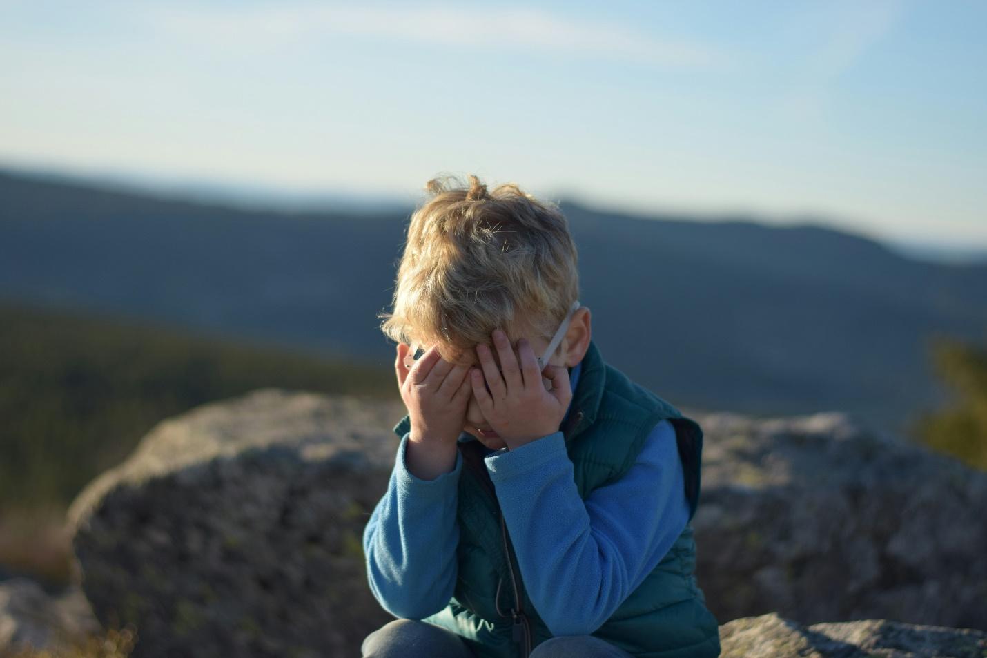 A child sitting on a rock with his hands in his face

Description automatically generated