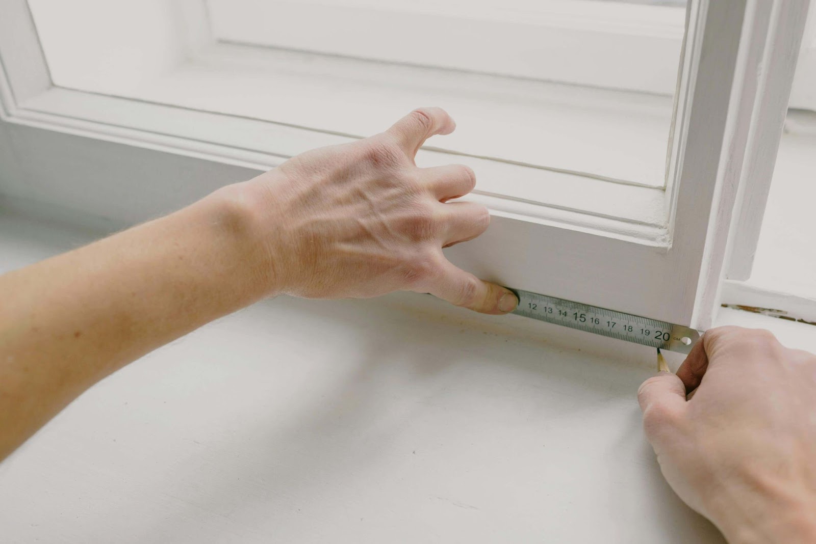 Man measuring the width of a window with a tape rule and pencil.