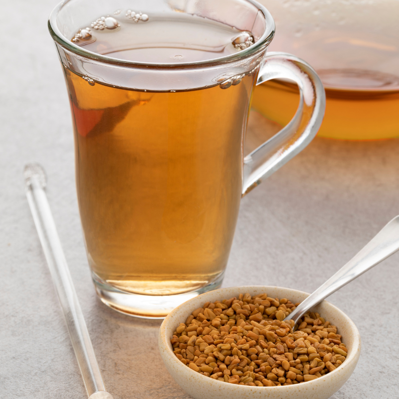 A glass cup filled with tea and a spoon beside it, featuring fenugreek leaves floating on the surface.