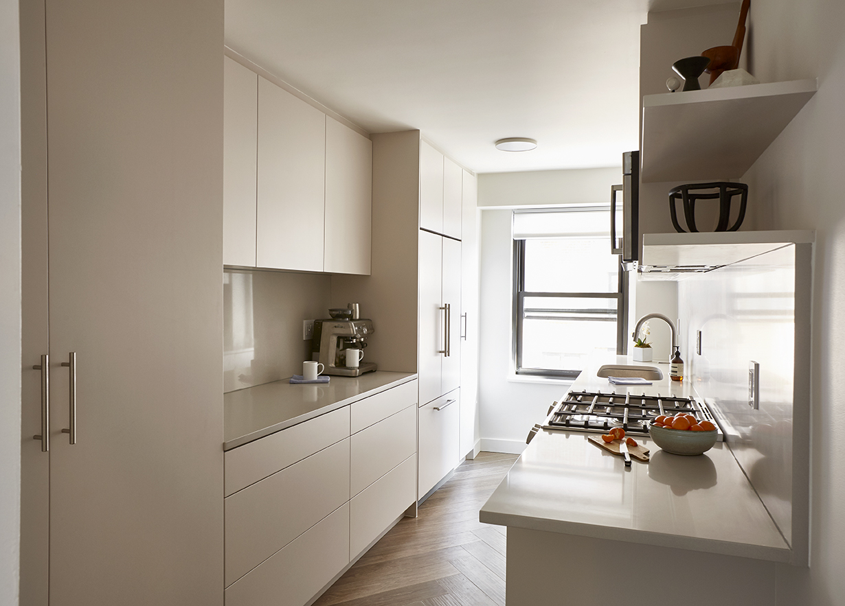 Narrow kitchen with hidden fridge matching white minimalist cabinets and countertops.