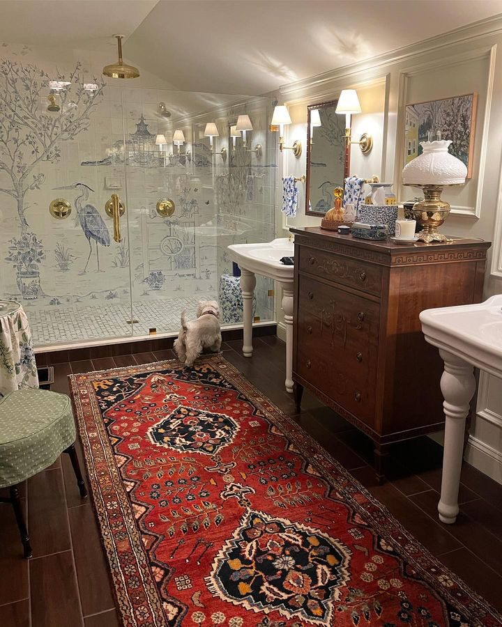 A brightly decorated traditional bathroom features porcelain pedestal sinks, chest of drawers, Persian rug and blue and white accessories