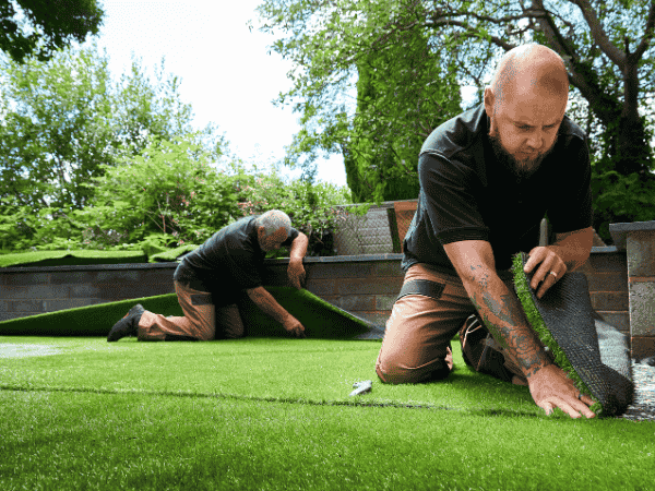 Workers installing artificial turf in a backyard, preparing the surface for infill to support turf structure and drainage.